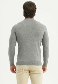 Pull en tricot gris avec un col et des manches côtelés, de coupe ajustée. Porté avec un pantalon beige, vu de dos.