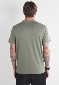 T-shirt en coton vert olive avec un col rond. Caractéristiques : manches courtes et un petit logo sur l'épaule gauche. Texture lisse.
