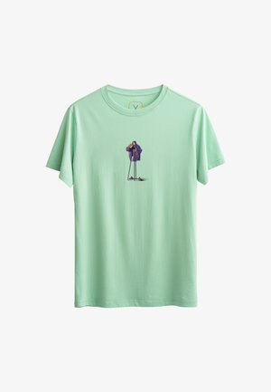 Lichtgroene katoen T-shirt met een centrale graphic van een persoon in een paarse jas die een camera vasthoudt, met zwarte broek en schoenen.