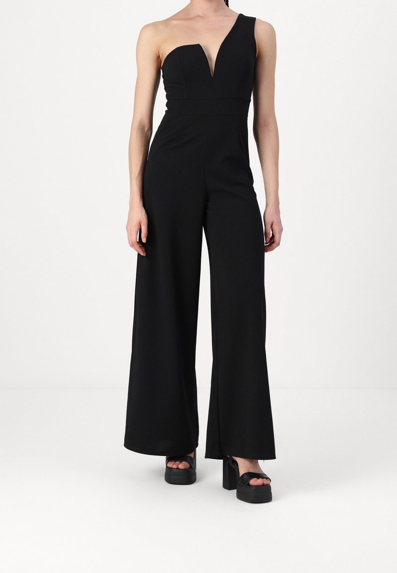 Svart jumpsuit med en axelrem, djup V-ringning, figurnära midja, vida ben och slät tyg; parat med svarta platåsandaler.