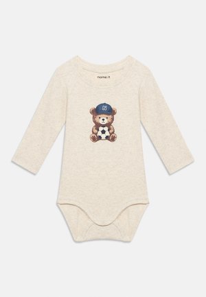 Bézs hosszú ujjú baba body, amelyen egy kék sapkás mackó látható, amint egy focilabdát tart a mellrészen nyomtatva.