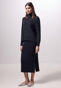 Dunkelblauer Strick-Turtleneck-Pullover mit geripptem Saum, kombiniert mit einem passenden, gerippten Midirock mit einem Schlitz an der Seite. Silberne Ballettschuhe vervollständigen den Look.