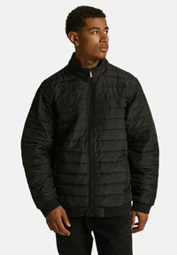 Czarna pikowana kurtka z wysokim kołnierzem, zamkiem błyskawicznym z przodu i ściągaczami przy mankietach. Gładka tekstura z poziomymi przeszyciami i małym logo.