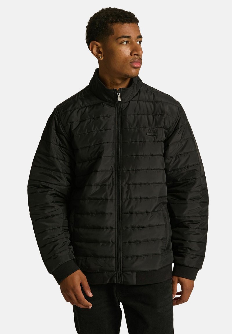 Czarna pikowana kurtka z wysokim kołnierzem, zamkiem błyskawicznym z przodu i ściągaczami przy mankietach. Gładka tekstura z poziomymi przeszyciami i małym logo.