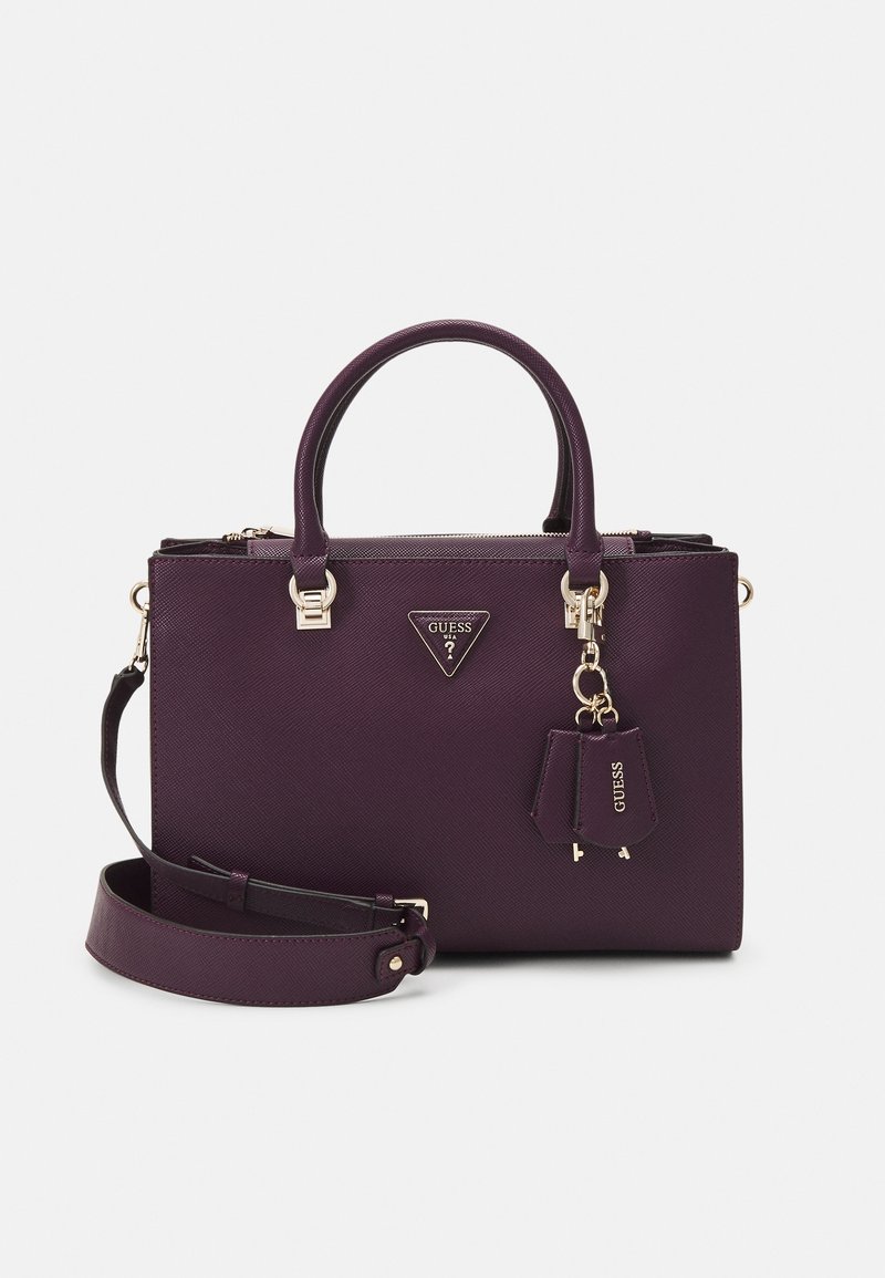 Sac à main Guess violet foncé avec doubles poignées, bandoulière amovible, ferrures dorées et porte-clés de marque suspendu à l'avant.
