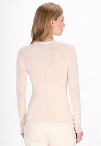 Lichtbeige longsleeve top van zacht, doorschijnend materiaal met een getailleerd design. Heeft een ronde halslijn en subtiele stikdetails.