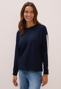 Sweatshirt en coton bleu marine avec des manches longues, présentant des rayures blanches sur les côtés et un col rond. Texture lisse et coupe décontractée.