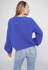 Blau gestreifter, übergroßer Strickpullover mit rundem Ausschnitt und fallenden Schultern. Kombiniert mit hellblauen, hoch taillierten Jeans.
