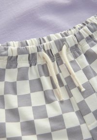 Karierte graue und weiße Stoff mit einem beigen Kordelzug, über einem einfarbigen lavendelfarbenen Abschnitt; elastischer Bund für verstellbare Passform.