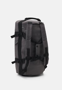 Grauer Rucksack aus strapazierfähigem Stoff, mit verstellbaren Trägern, Schnallen und einem minimalistischen Design. Enthält seitliche Taschen und ein Logo-Detail.