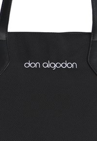 Bolsa tote negra con tejido texturizado, que cuenta con dos asas negras y el logo blanco "don algodon" centrado en la parte frontal.