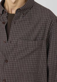 Chemise à carreaux brun avec un col boutonné, une poche sur le côté gauche de la poitrine et un motif de grille blanche contrastant. Fabriquée en tissu léger.