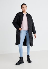 Mustmustriibuline must pikka jope, millel on sooniline krae, kantud heleda roosa kudumi sviitri peal, koos helesiniste teksade ja mustade nööriga saappastega.