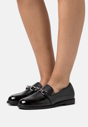 Mocassins en cuir verni noir avec un détail en chaîne argentée brillante, semelle plate, bout rond et finition lisse.