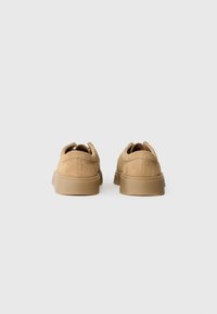 Pantofi din suede bej cu un design cu profil redus și spate rotunjit. Au o talpă din cauciuc și detalii de cusătură minime.