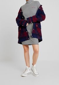 Kurtka w kratę w granatowym i burgundowym kolorze na czarno-białej sukience w paski, zestawiona z białymi trampkami za kostkę. Prosty design, casualowy look.