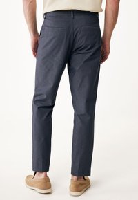 Granatowe spodnie slim-fit z teksturowanego materiału, z tylnymi kieszeniami i średnim stanem, połączone z beżowymi butami typu slip-on.