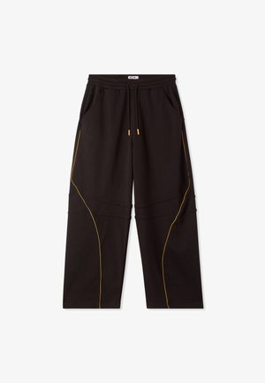 Pantaloni da tuta neri a gamba larga con vita elasticizzata, cordoncino, tasche laterali e dettagli in piping giallo lungo le gambe.