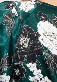 Floral blouse featuring a teal and black satin fabric, with white and gold-accented floral patterns and smooth texture.