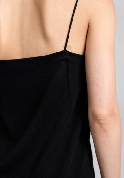 Top senza maniche nero con spalle sottili, delicata al tatto e dalla vestibilità rilassata, che si adagia sulla spalla, esponendo la pelle e un piccolo tatuaggio.