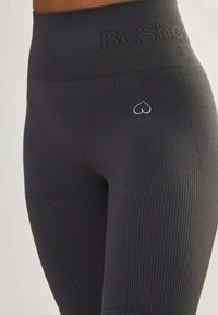 Hoge zwarte leggings met ribbeltextuur, voorzien van een klein hartlogo en "BeShap" branding op de tailleband voor extra detail.