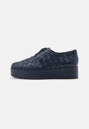 Chaussure à plateforme en cuir bleu marine avec un design tissé et des lacets noirs, vue de côté sur fond blanc.