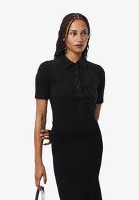Polo negro de manga corta en material texturizado con un cierre de botones en la parte delantera y un bolsillo en el pecho, combinado con una falda negra ajustada de canalé.