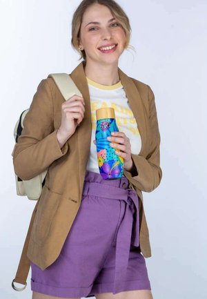 Genanvendelig vandflaske med et blåt og livligt blomstermønster, cylindrisk form og gul låg, holdt af en person i en tan blazer og lilla shorts.