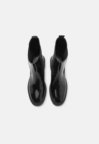 Botines de charol negro con acabado liso, paneles laterales elásticos y punta redondeada. Suela gruesa de goma para mayor estabilidad.