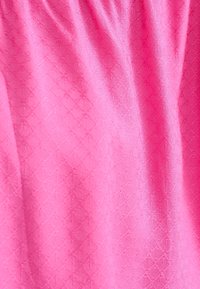 Tissu rose avec un motif subtil en losanges et des plis doux créant des ombres délicates et une texture sur la surface.