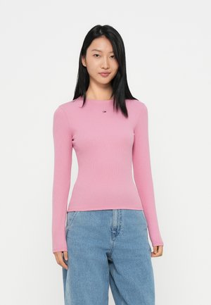 Haut en rib haut à manches longues, rose, avec un col rond et un petit logo sur la poitrine, associé à un jean en denim bleu clair à coupe ample.