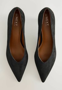Svarta mocka pumps med spetsig tå, sl�ät yta, låg skärning och bruna läderinsåler. Har minimal logotyp på insålen.