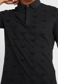 Černé polo tričko z bavlněné směsi s vzorovaným designem, vyraženými logy a hvězdami, s límečkem a zapínáním na dva knoflíky.