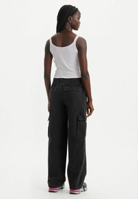 Pantaloni cargo neri con una vestibilità ampia, dotati di tasche laterali e una vita alta, abbinati a una canotta bianca. Tessuto a trama.