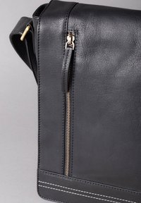 Black leather messenger bag featuring a textured finish, gold zipper, and white stitching details along the base. Compact and functional design.