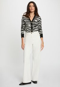 Cardigan en tricot rayé noir et blanc avec un décolleté en V et des boutons dorés, associé à un pantalon large taille haute blanc et des ballerines noires.