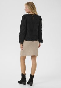 Sort broderet langærmet top med bølget kant, parret med en beige strikket nederdel og sorte hælstøvler. Bagview vist.