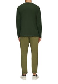 Donkergroene blouse met lange mouwen, gecombineerd met olijfgroene broek. Witte sneakers met blauwe accenten, met een eenvoudige en losse pasvorm.
