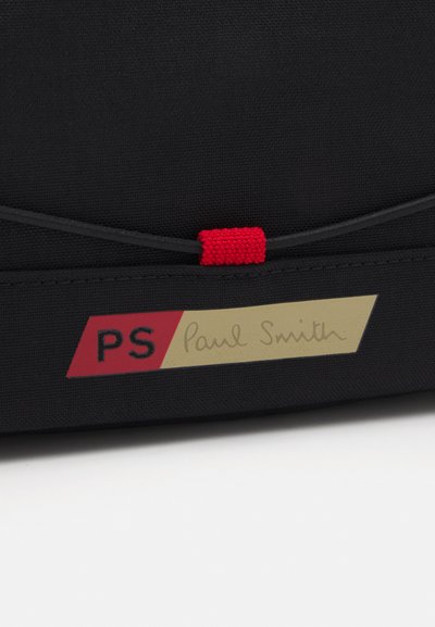 Borsa di stoffa nera con una superficie testurizzata, un tassello di accento rosso e un'etichetta logo oro e rossa con la scritta "PS" e "Paul Smith."