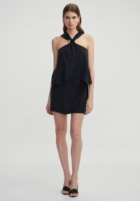 Schwarzes ärmelloses Kleid mit einem geknoteten Neckholder-Oberteil und geschichtetem Saum. Hergestellt aus glattem Stoff, mit einem taillierten Oberteil und ausgestelltem Schnitt.