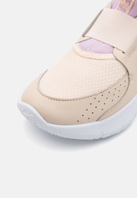 Beige színű sportcipő, amely hálós és sima szintetikus anyagokból készült, jellegzetes perforációkkal, széles pánttal és fehér gumitalppal rendelkezik.