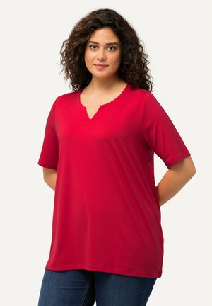 Rotes kurzärmeliges V-Ausschnitt-T-Shirt aus weichem, glattem Stoff. Hat eine lockere Passform und einen abgerundeten Saum, kombiniert mit dunkelblauen Jeans.