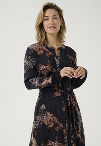 Tume navy sinise pika varrukaga kleit keerukate paisley-mustritega pruunides ja sinistes toonides. Erakordne nööpidega esitamine ja sobiv riidest vöö.