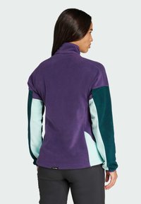 Paarse fleec jacket met teal en lichtblauwe accenten. Bevat een hoge kraag en een textuurfabric, ontworpen voor comfort en warmte.