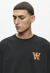 Zwarte katoenen T-shirt met een oranje "W" logo op de linkerkant van de borst. Ronde hals en een ontspannen pasvorm met korte mouwen.