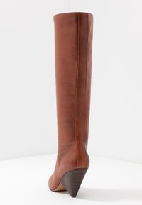 Botte haute jusqu'au genou en cuir marron avec un talon compensé effilé, une texture lisse et un détail de couture courant le long de l'arrière.
