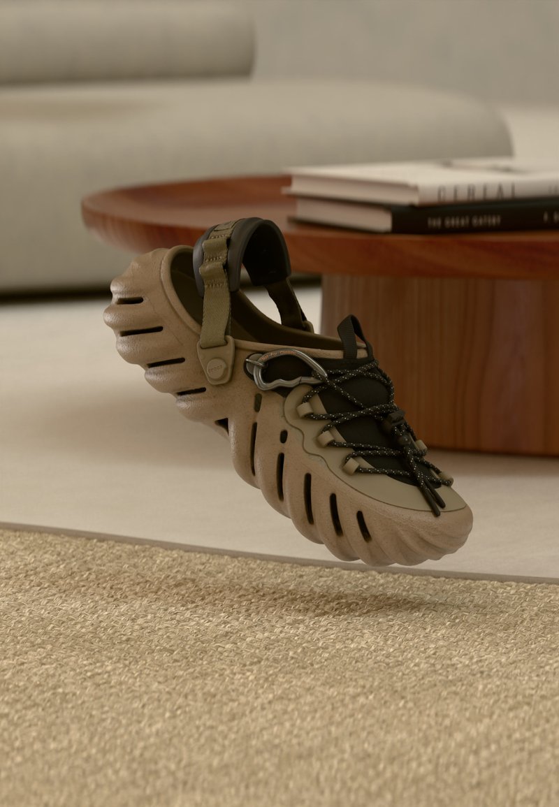 Μπεζ και μαύρο σανδάλι με ανοιχτή πίσω πλευρά, παχιά υφή στη σόλα, ρυθμιζόμενο λουράκι και μαύρα κορδόνια, τοποθετημένο κοντά σε ξύλινο τραπέζι με στοιβαγμένα βιβλία.