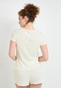 Haut jaune clair à manches courtes et shorts assortis en texture côtelée. Présente des bords ondulés et une coupe décontractée, avec de légères rayures verticales.