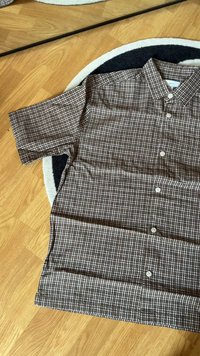 Chemise à manches courtes à boutons, en motif carreaux marron et blanc, fabriquée en tissu tissé, avec un col pointu et cinq boutons.