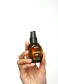 Sérum Aveda Tulasara Calm dans un flacon en verre ambre avec une pompe noire. L'étiquette présente un texte blanc avec le nom du produit et sa description.